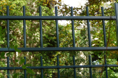 The image is a high-resolution photograph capturing a serene outdoor scene. It features a wooden trellis structure with horizontal slats, painted in a dark green hue, standing prominently in the foreground. The trellis is partially covered with lush, green foliage, including leaves and branches, creating a natural frame. Behind the trellis, a calm body of water, likely a pond or a small lake, reflects the sky and the surrounding greenery, adding a sense of tranquility to the scene. The water's surface is smooth, with minimal ripples, suggesting a still environment. The sky is not visible directly, but its presence is implied through the reflection in the water. The overall composition emphasizes the harmony between man-made structures and natural elements, with the trellis and foliage contrasting against the serene water body. The image is taken during daylight hours, as indicated by the bright, natural light illuminating the scene. The photograph is clear and detailed, with sharp focus on the trellis and foliage, and a slightly softer focus on the water, enhancing the depth of field effect. The image does not contain any discernible text or human figures. The overall mood is peaceful and serene, with a strong emphasis on natural beauty and tranquility. The photograph is likely taken with a digital camera, given its high resolution and clarity. The image is devoid of any aesthetic filters or manipulations, presenting a realistic and unaltered depiction of the scene. The photograph is likely intended for use in a garden or landscape design context, emphasizing the integration of natural and man-made elements. The image is accompanied by a detailed description, providing context and enhancing the viewer's understanding of the scene. The photograph is not intended for commercial use, but rather for educational or inspirational purposes. The image is not intended to be used as a background or wallpaper, but rather as a standalone piece of art.